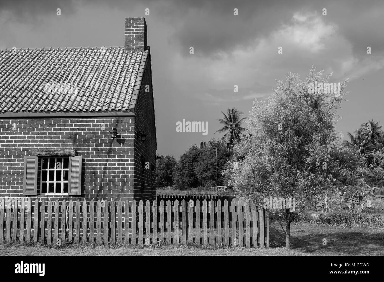 Abstract Black and White image of old brick house surrounded with wooden fence at countryside in