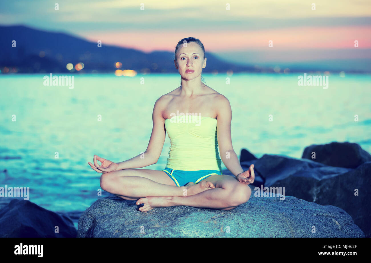Young girl in yoga pose lotos at ocean quay Stock Photo - Alamy