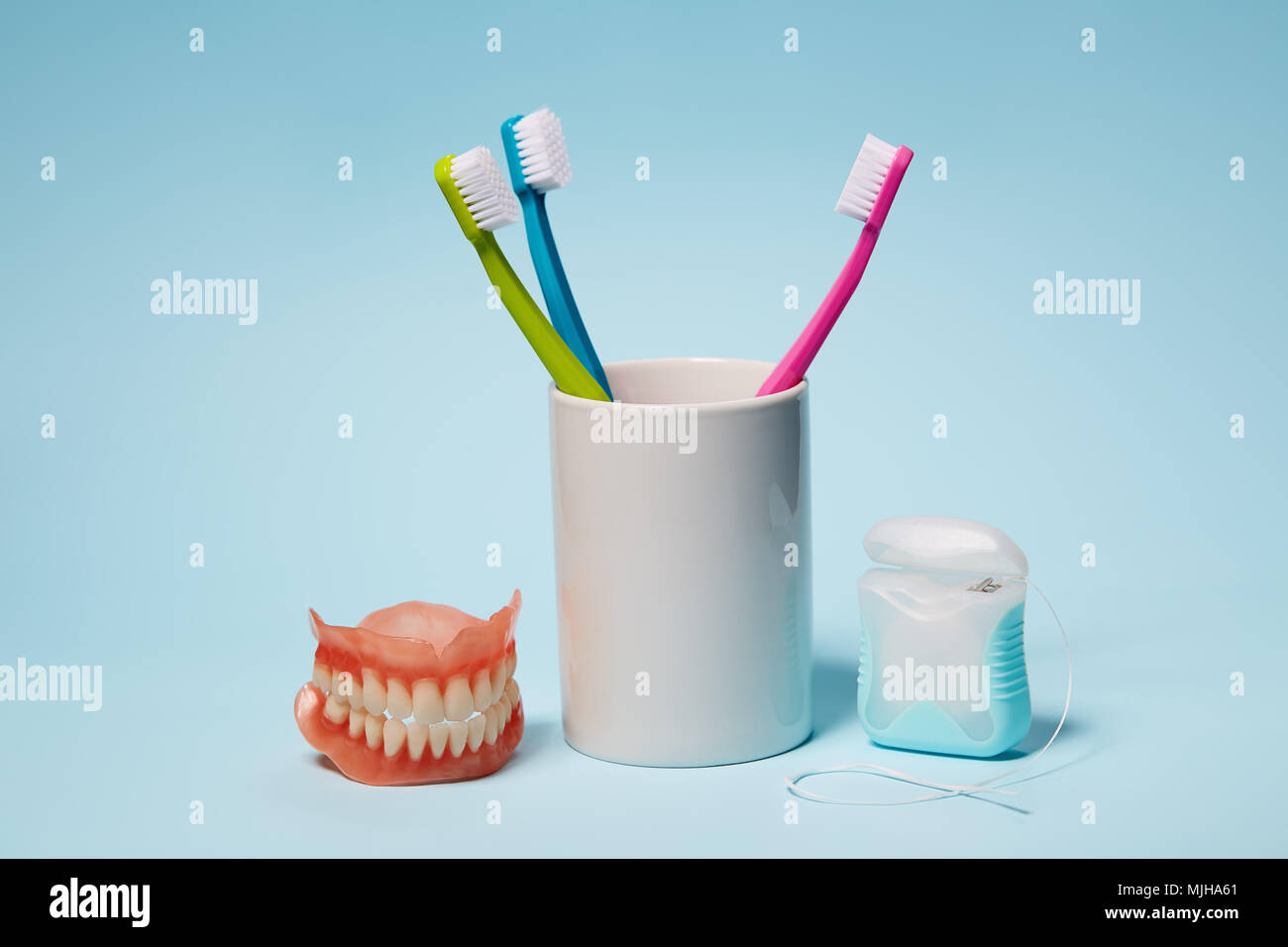 Dental Equipment. Colorful toothbrushes, dentures and dental floss on light blue background. Stock Photo