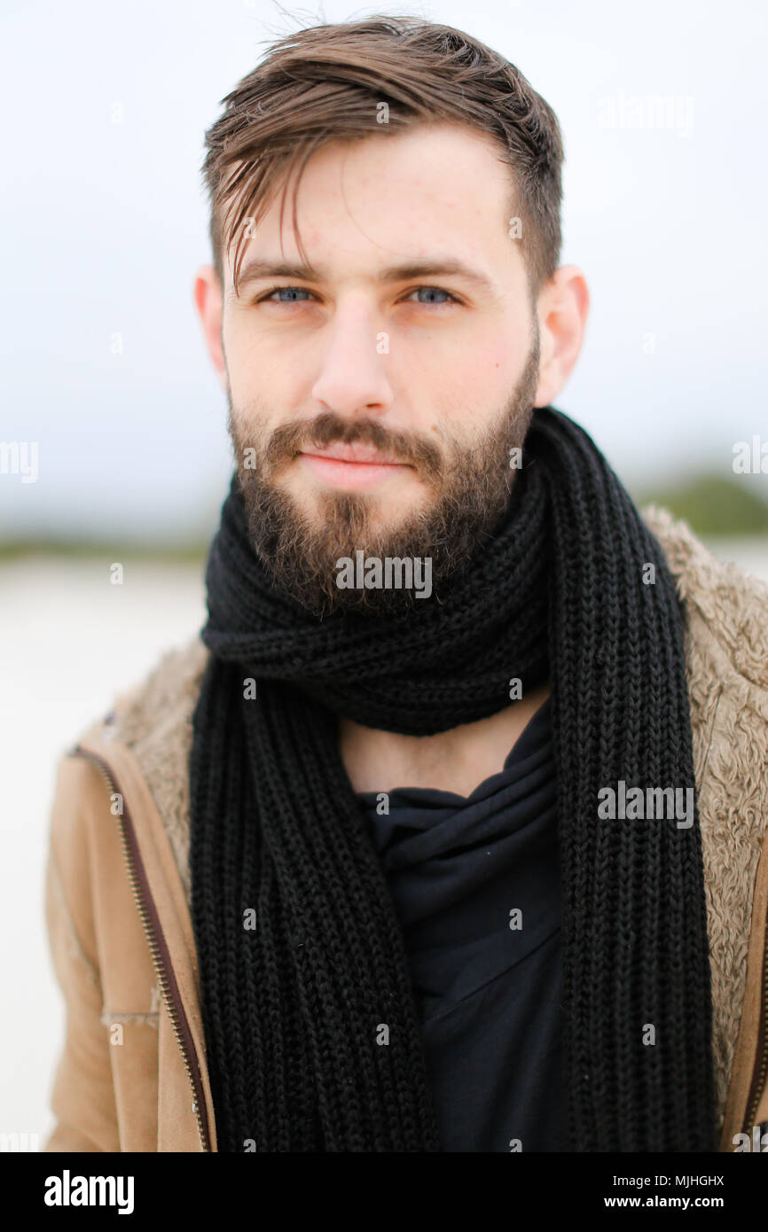 Close up portrait of young man with beard wearing coat and black scarf ...