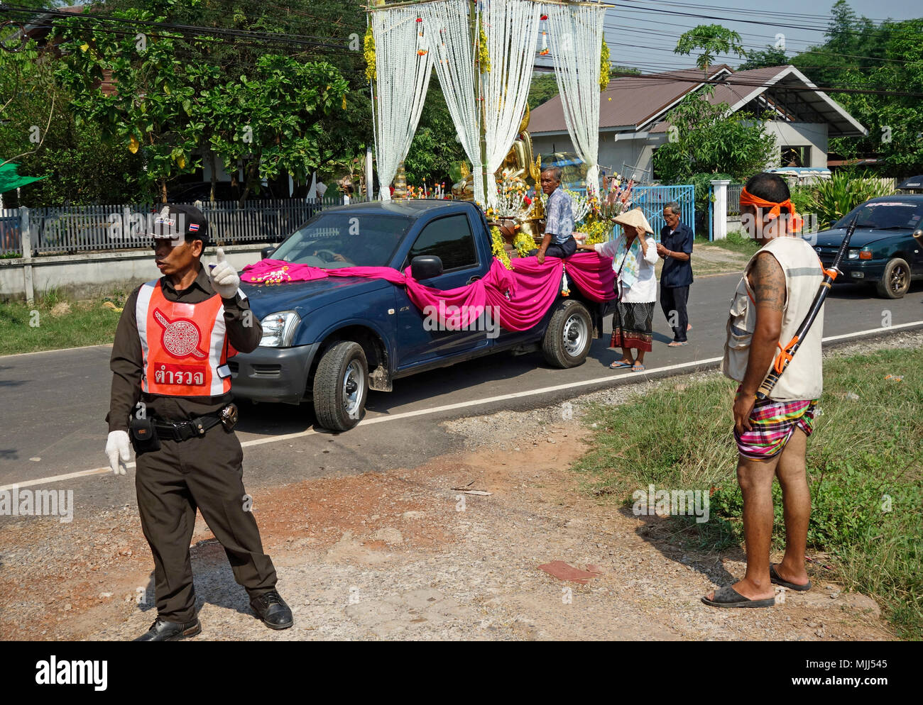 Songkran Thai New Year, policeman controls traffic for pickup truck carrying golden Buddha statue, monk and decorations, Udon Thani, Isaan, Thailand Stock Photo