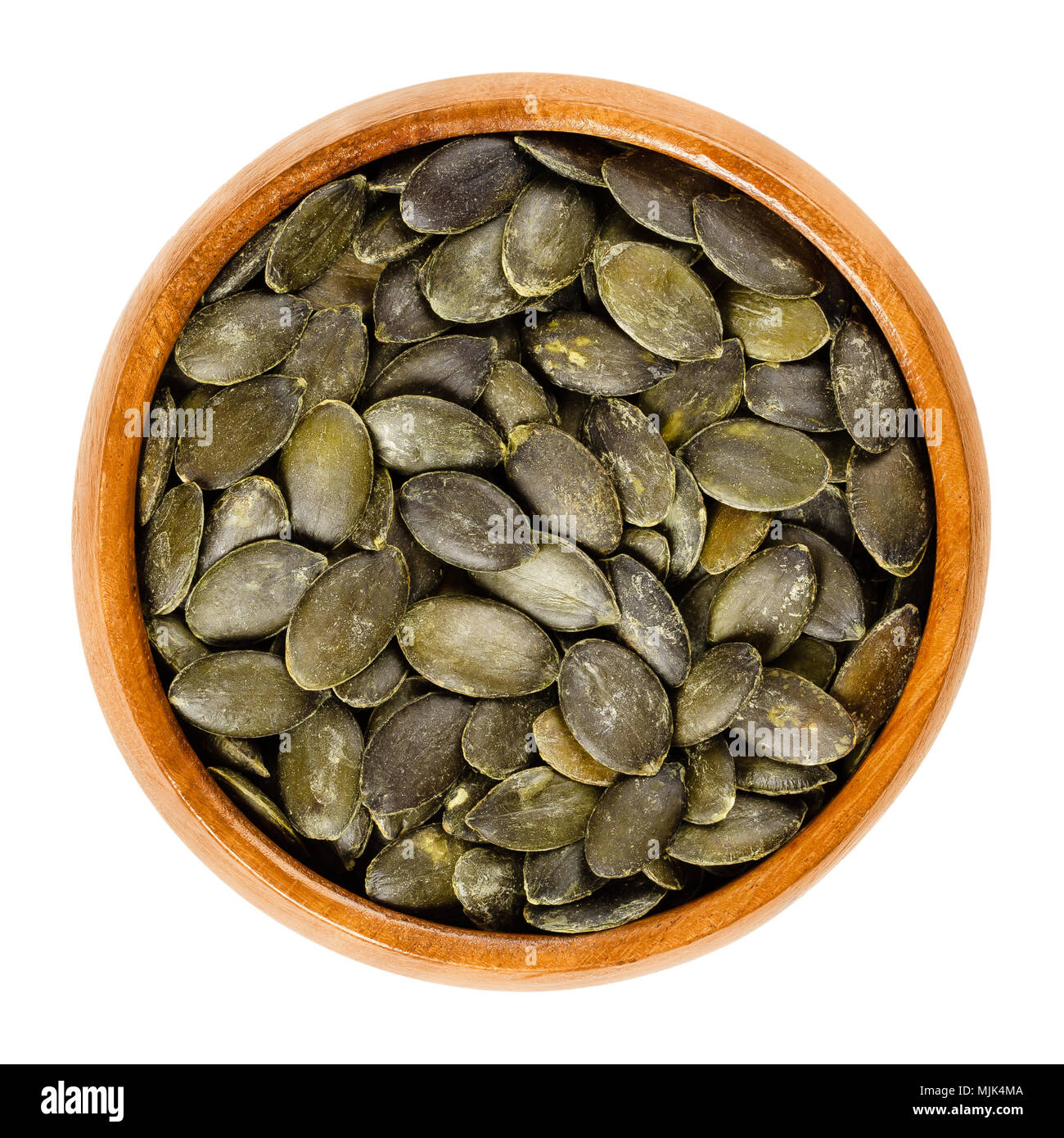 Roasted and salted pepita pumpkin seeds in wooden bowl, used as snack. Flat green edible summer squash seeds of Cucurbita pepo. Isolated macro photo. Stock Photo