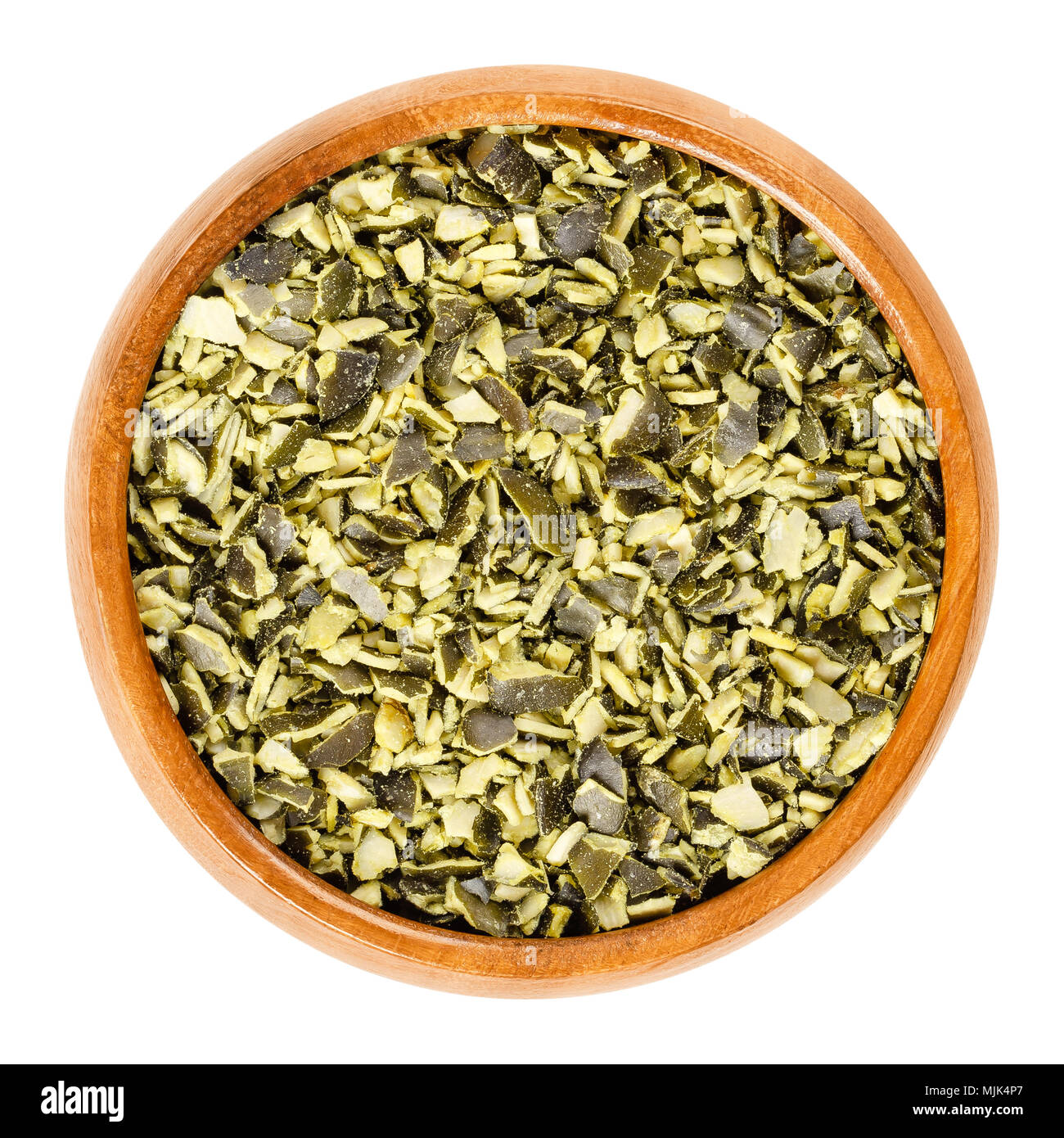 Roughly chopped raw pepita pumpkin seeds in wooden bowl, used for cooking. Flat green edible summer squash seeds of Cucurbita pepo. Stock Photo