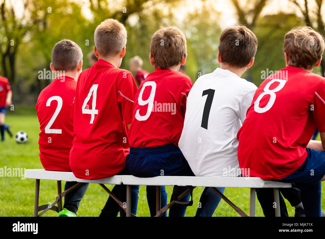 Kids Soccer Team Players Sitting on a Bench on a Sunny Day. Children Football Team Players. Young Boys Watching Soccer Match. Youth Footballers of Soc Stock Photo