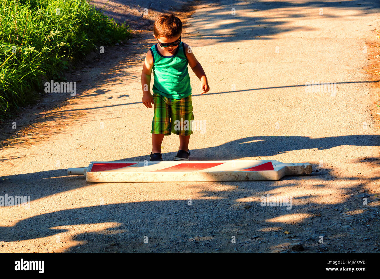 Little boy is carrying a construction site barrier across the street. To overcome difficulties Stock Photo