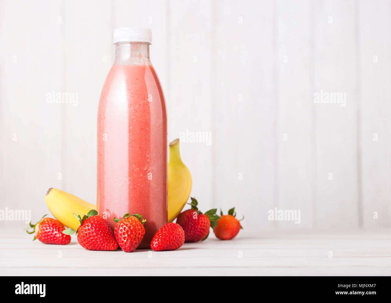 Plastic bottle with fresh summer berries smoothie on wooden background.Strwberry and banana flavour. Stock Photo