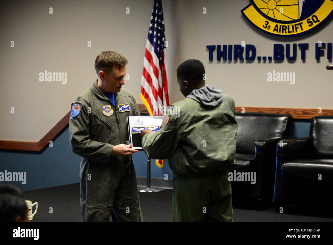 Lt. Col. Mark Radio, 3rd Airlift Squadron commander, holds the Pilot for a Day plaque while Kareem Bennett affixes his nametape to it during a squadron roll call March 16, 2018, at Dover Air Force Base, Del. Flying squadrons traditionally hold a ceremony for outgoing or retiring members that involves placing their nametape on a board to commemorate their service to the organization. Armed Forces and civilians displaying courage bravery dedication commitment and sacrifice Stock Photo