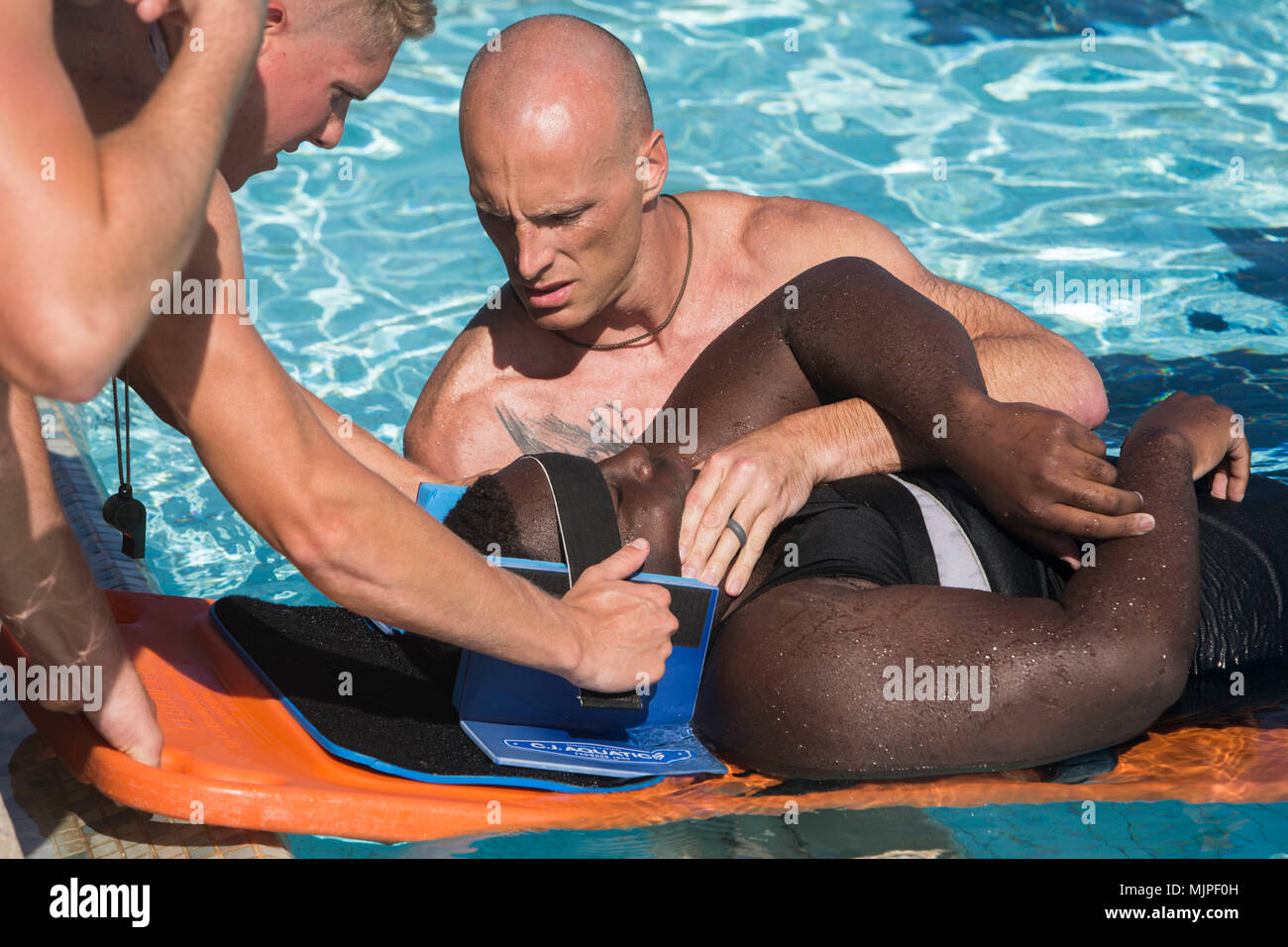 U.S. Marines attending a Marine Corps Instructor of Water Survival (MCIWS) course strap down a simulated victim to a lifeguard spinal board at the base pool, Marine Corps Base Hawaii, Dec. 13, 2017. MCIWS gives Marines and Sailors the necessary skills to respond to emergency situations in aquatic environments, and allows them to oversee annual swim qualifications. (U.S. Marine Corps photo by Lance Cpl. Isabelo Tabanguil) Stock Photo