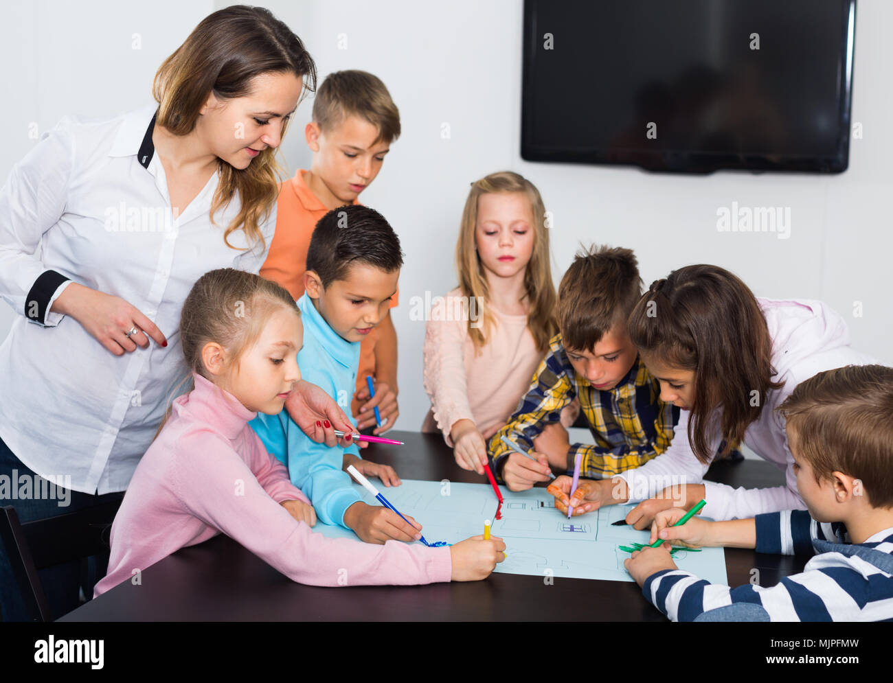 Little cute smiling children with teacher drawing together in classroom ...