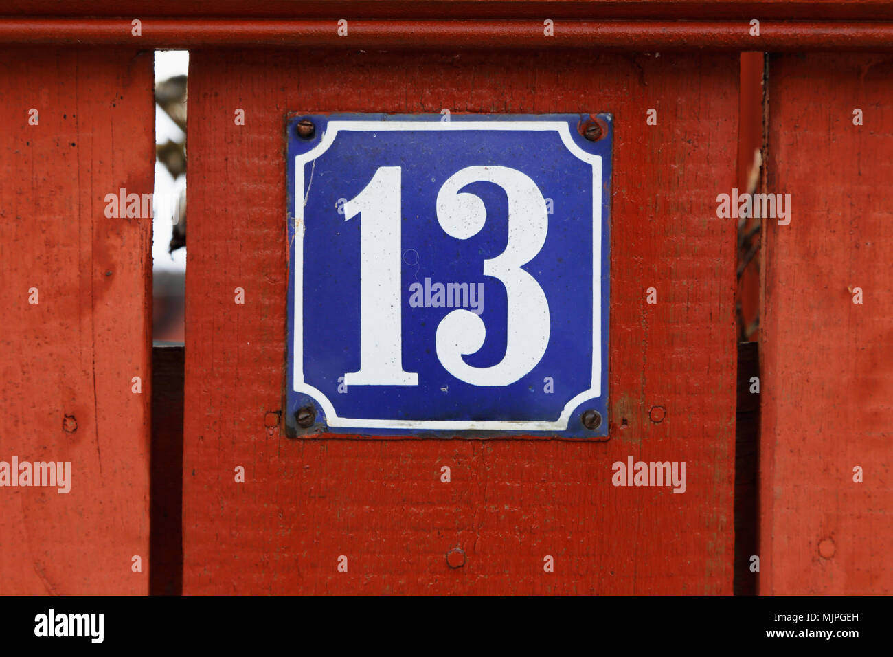 House number thirteen on blue background mounted on red wooden fence. Stock Photo