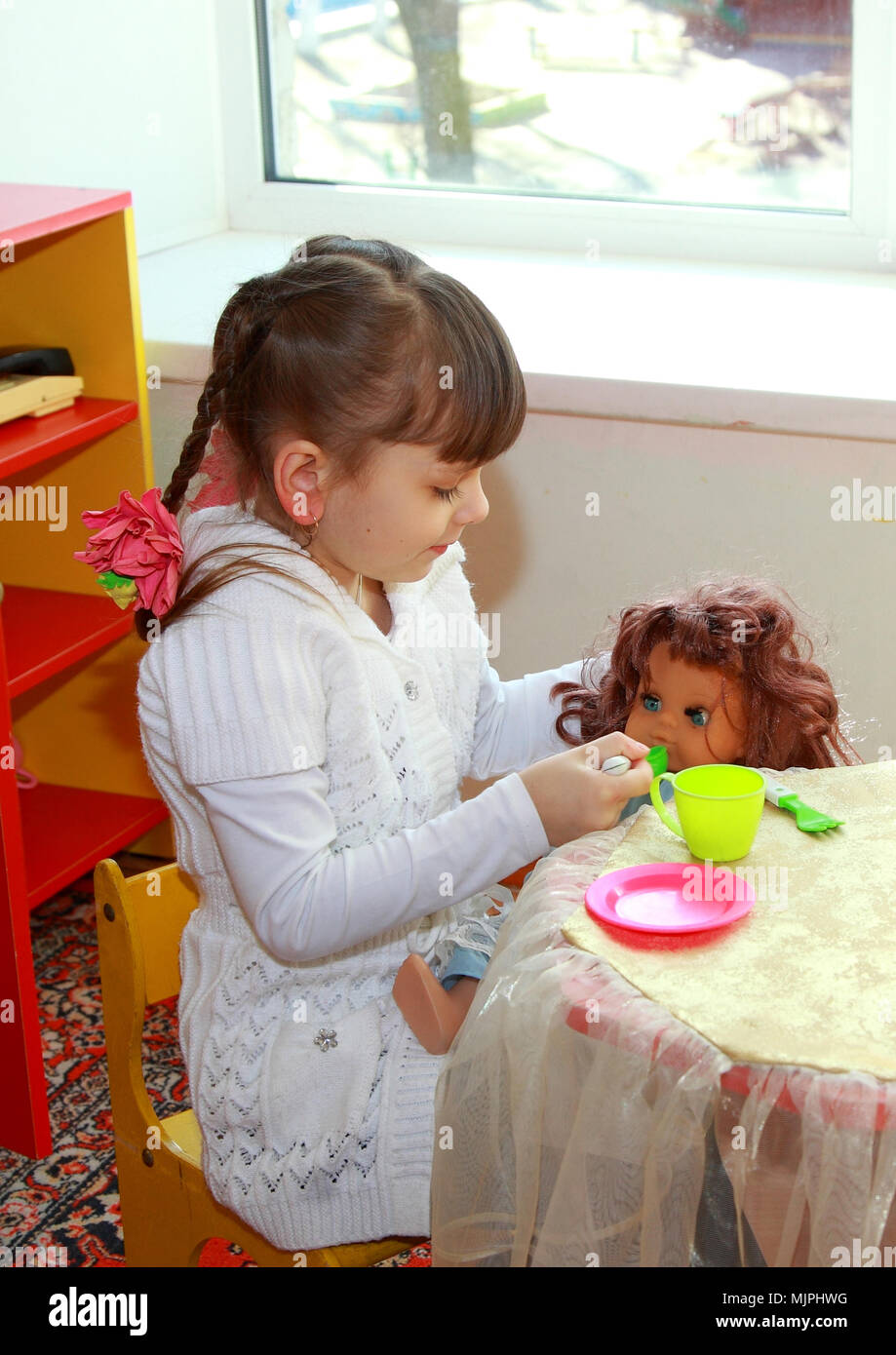 Child in kindergarten. The little girl feeds the doll. Stock Photo