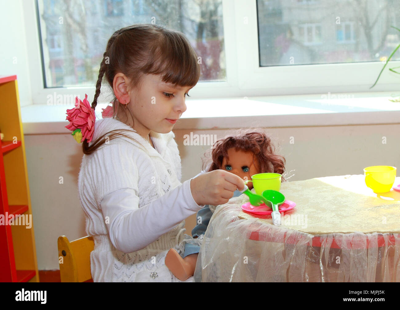 Games in kindergarten. The girl feeds her doll. Stock Photo