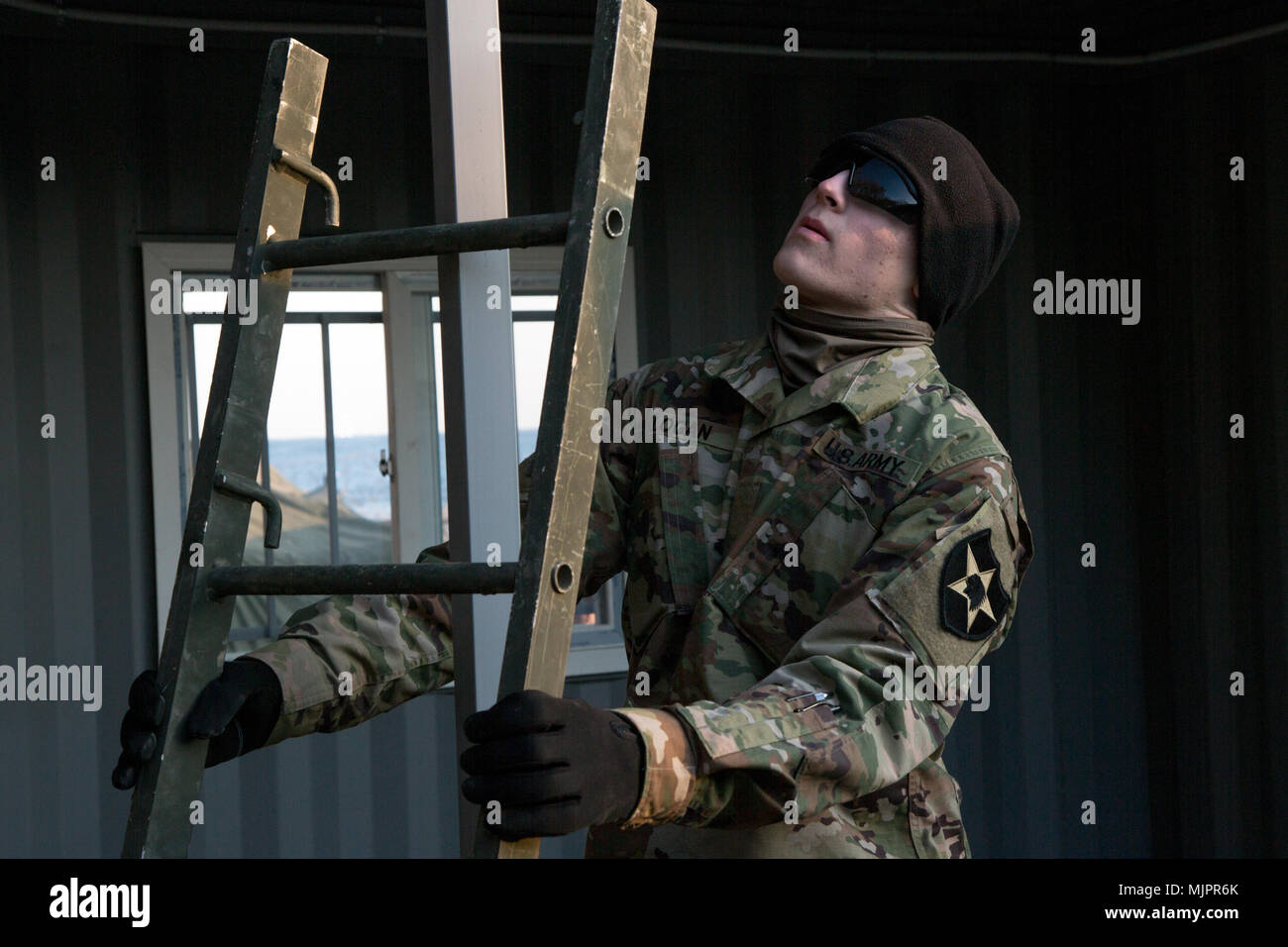 U.S. Army Soldier, Vertical PLT, 643rd ESC, 11th Engineer Battalion holds ladder into place in South Korea, Dec. 14, 2017. A conex box was created during the Korean War and is used for accomendations for soldiers. (U.S. Army photo by Pfc. Isaih Vega) Stock Photo