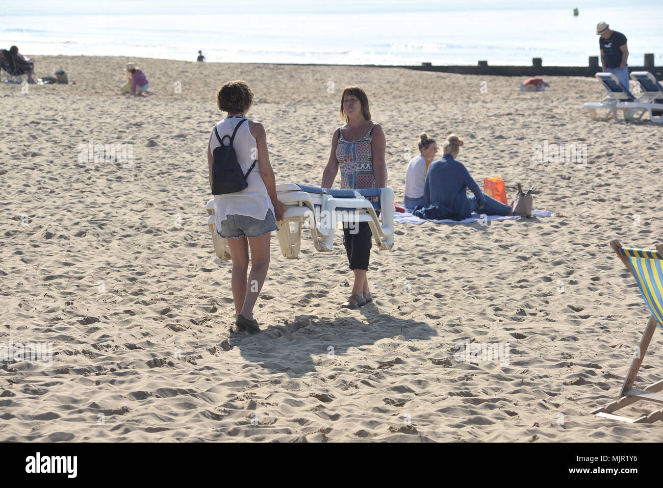 Boscombe, Bournemouth, Dorset, UK, 6th May 2018, Weather: Morning sunshine on the south coast on what could be the hottest Mayday bank holiday weekend on record. Two women carrying sunbeds onto the beach. Stock Photo