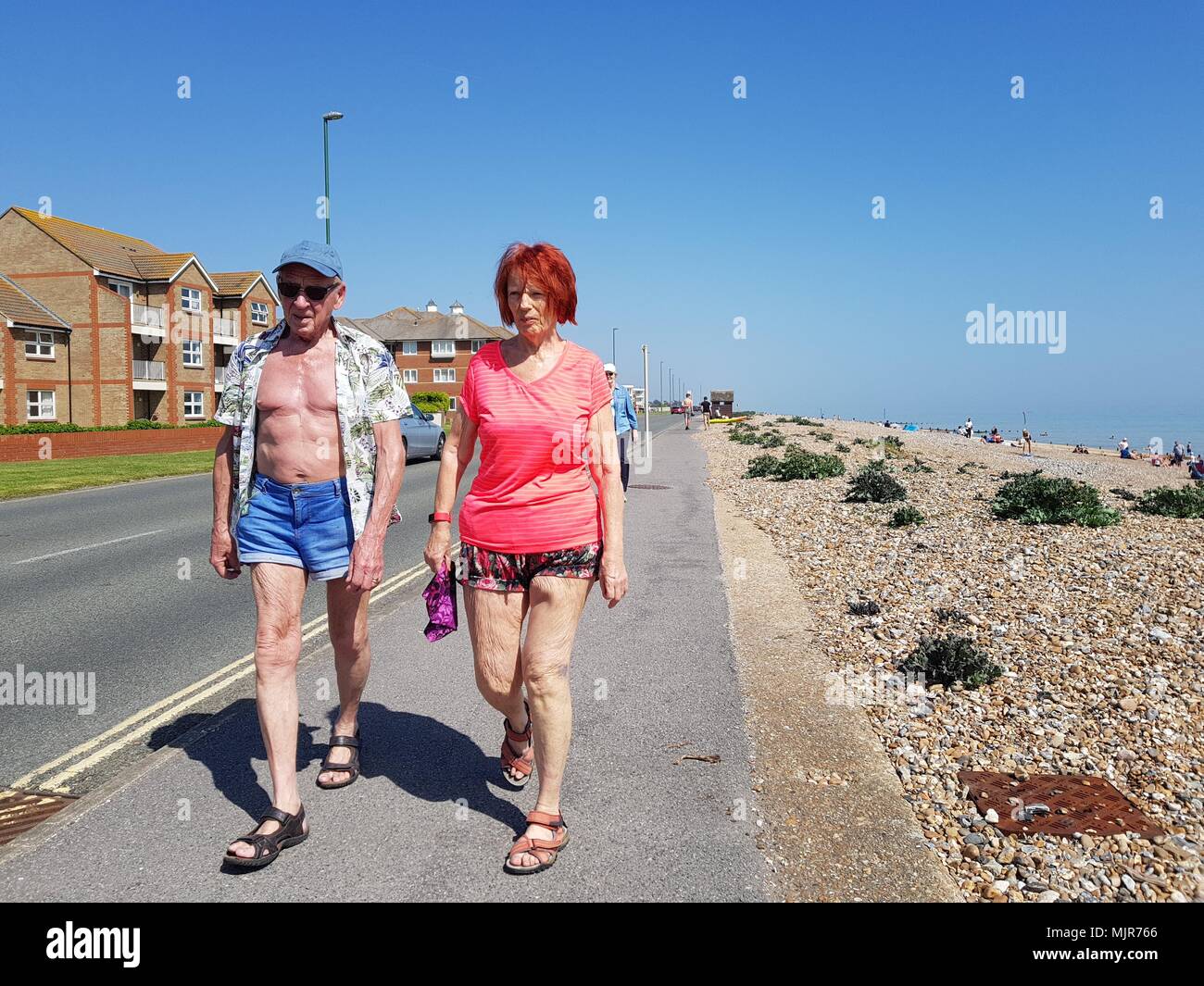 A couple enjoying an afternoon stroll along the seafront road on a hot and sunny day during the Spring 2018 heatwave, on the South Coast in the UK. Stock Photo