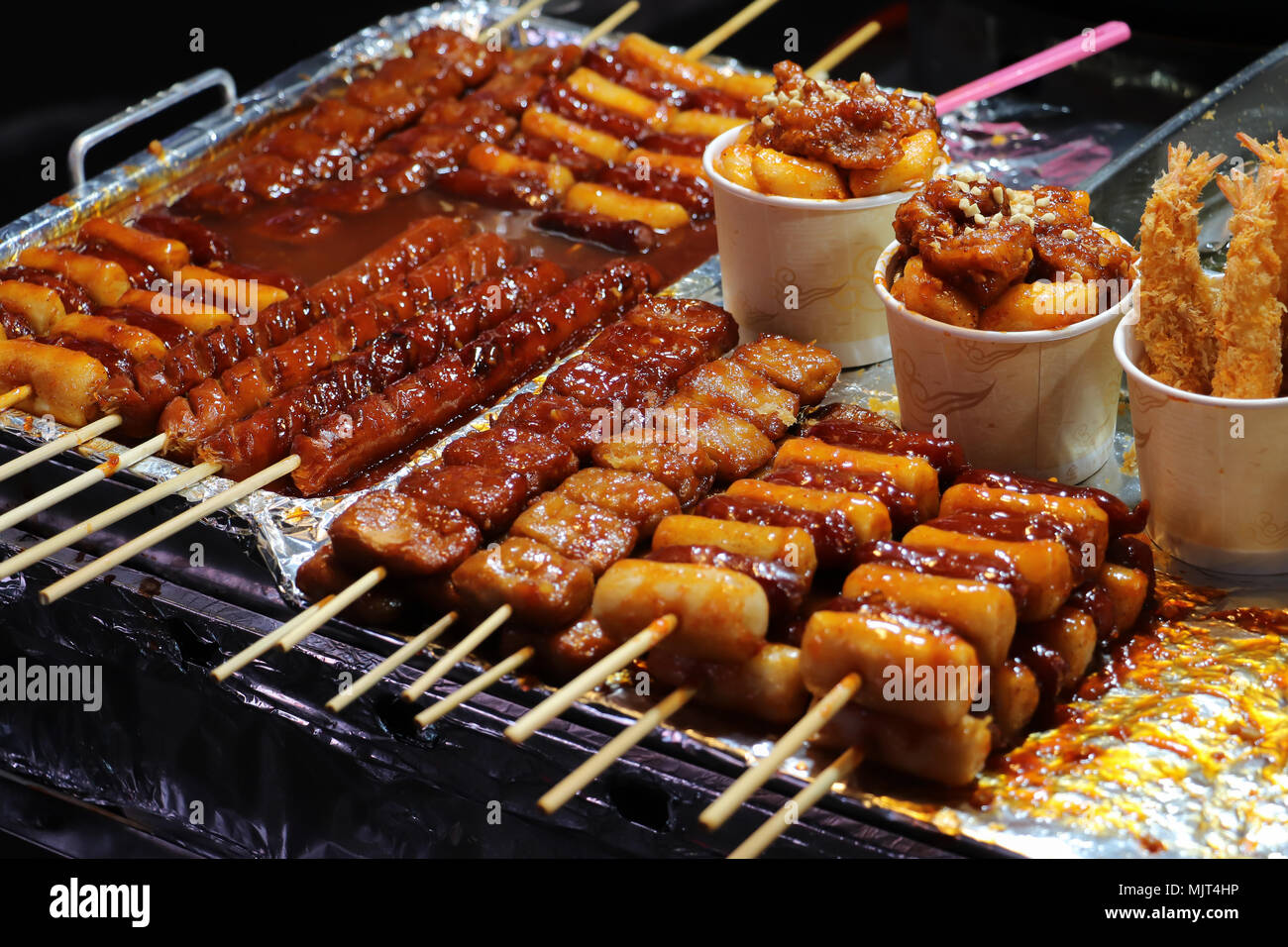 Closeup of sausages and meat on wooden skewers, covered with a red