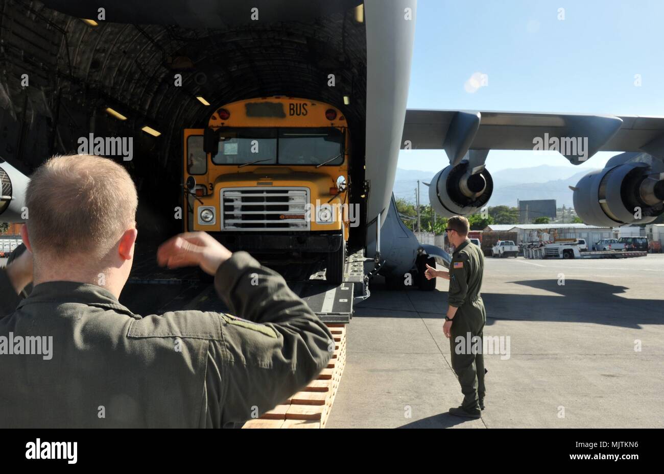 Staff Sgt. Paul Sizemore, loadmaster with Joint Base Charleston's 317th Airlift Squadron, left, with assistance from Capt. Gus Morse, guides the offloading of school buses from a C-17 aircraft in Port-au-Prince, Haiti, December 16, 2017. The buses are destined for a local school run by outreach organizations Those Angels Foundation and Sister Cities International, and were transported as part of the Denton program, which allows for space available on military aircraft to be used for humanitarian cargo. (U.S. Air Force photo by Capt. Justin Clark) Stock Photo