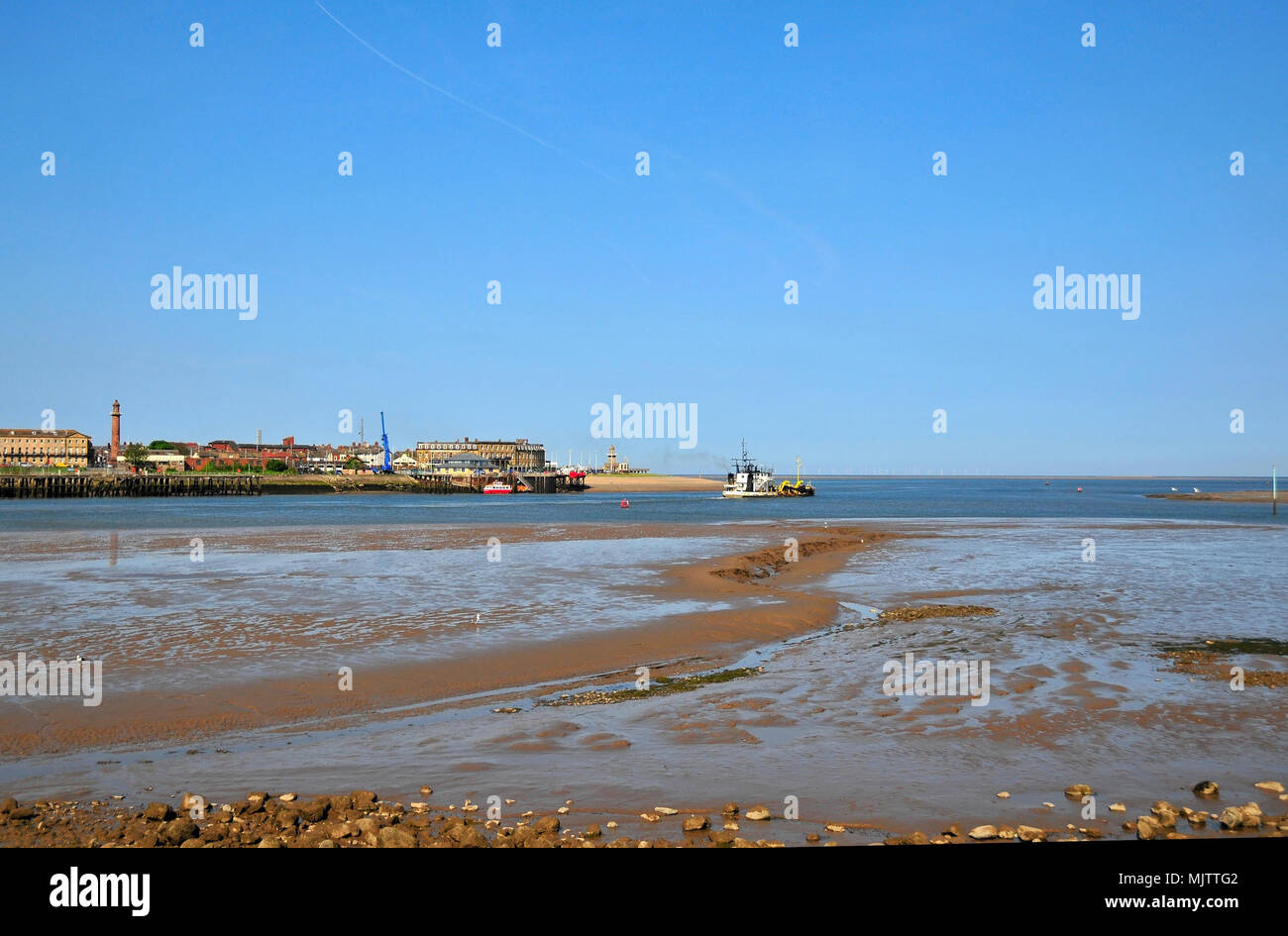 Blue sky wet beach view to dredger moving out to sea River Wyre Channel from Knott End to Fleetwood lighthouses and buildings, Lancashire, UK Stock Photo
