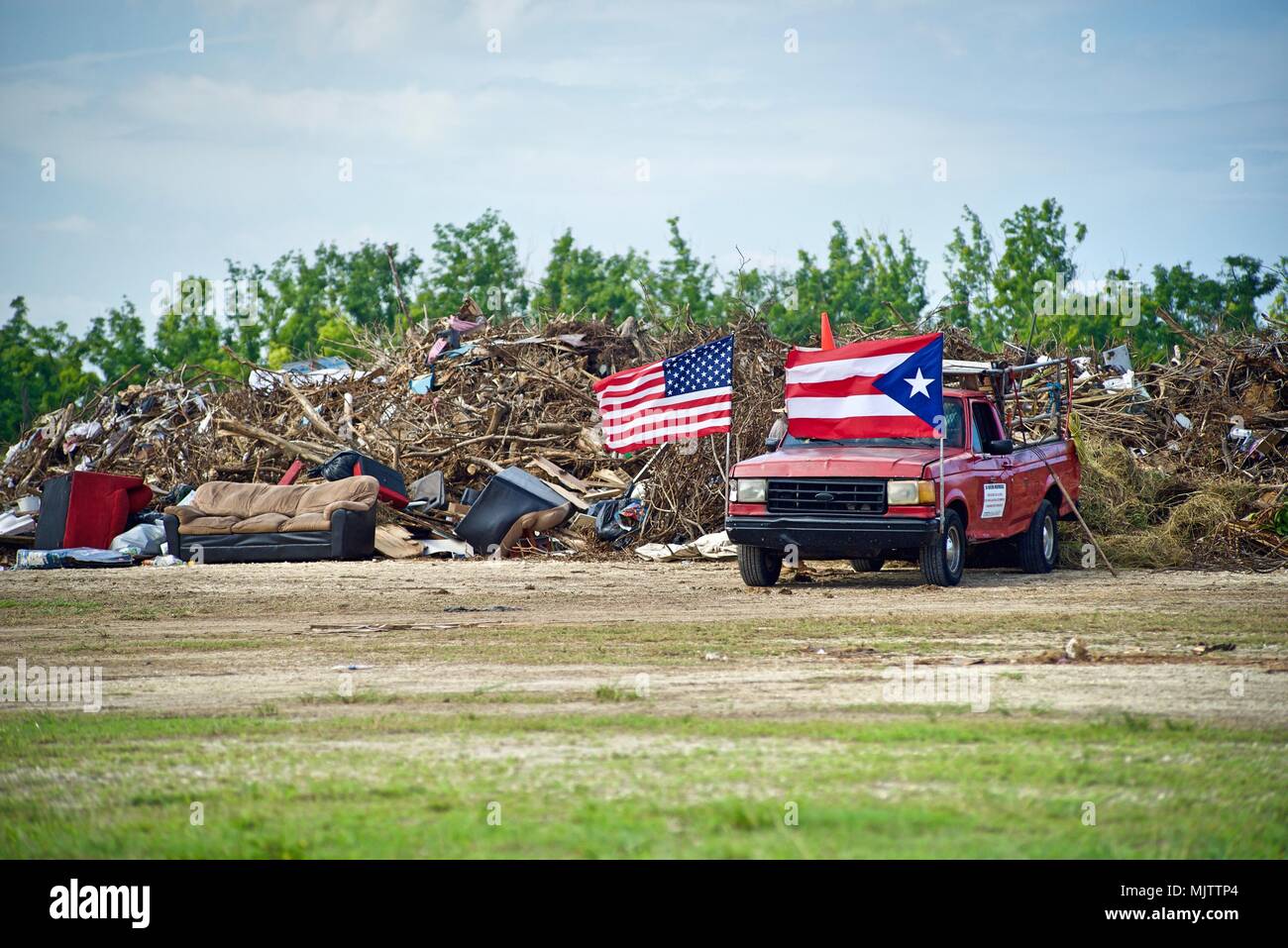 BARCELONETA, Puerto Rico, December 12, 2017 – Puerto Rico and U.S. flags  wave in front of a massive debris drop-off site in Barceloneta. Couches,  televisions, refrigerators, toys, clothing, and books were among