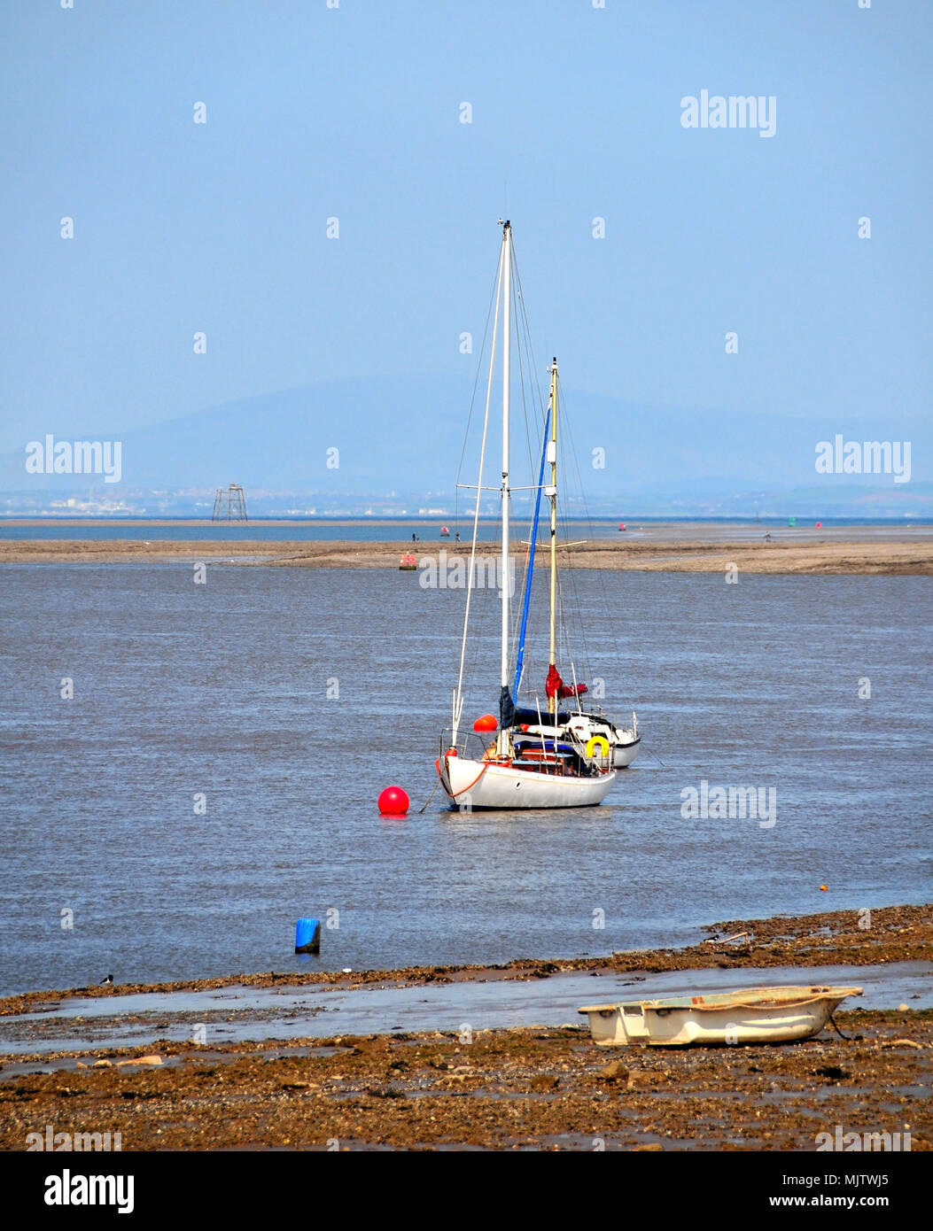 Blue sky portrait, west to Wyre Light and Black Combe, of beached rowing boat, two yachts anchored at the River Wyre mouth, Knott End, Lancashire, UK Stock Photo