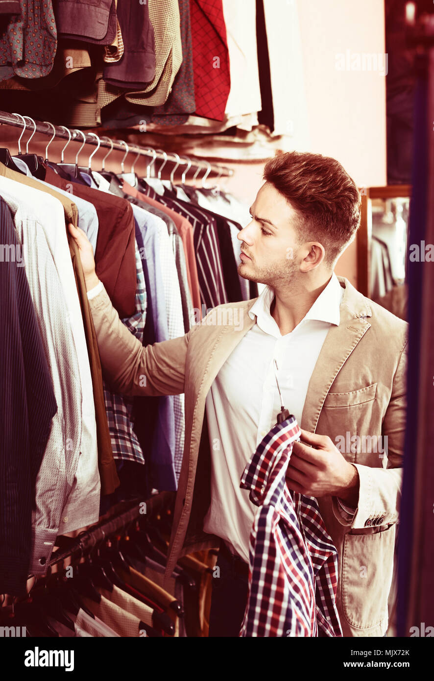Positive young man choosing new shirt in men’s clothes store Stock ...