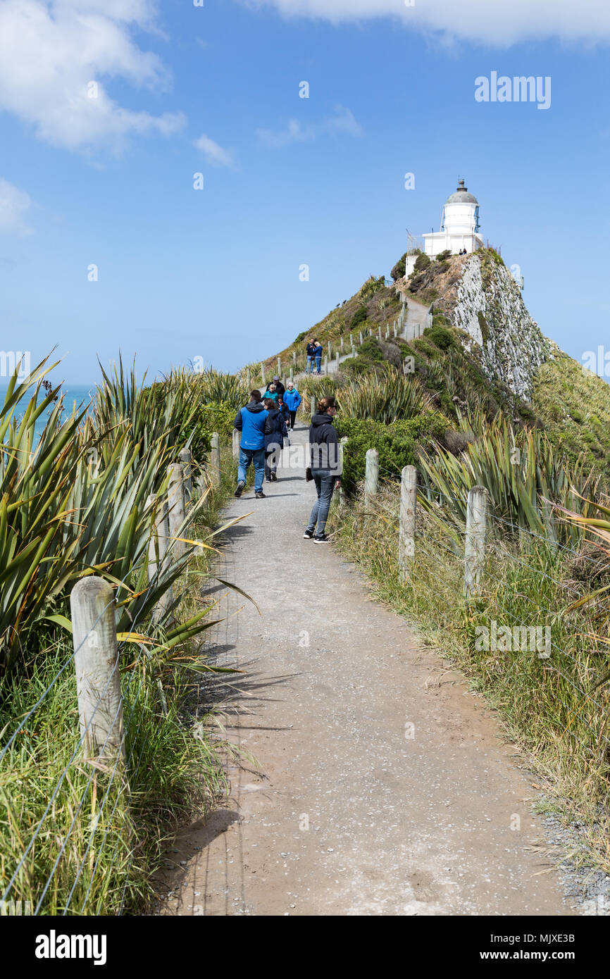 CATLINS COAST, NEW ZEALAND - NOVEMBER 11, 2017: Visitors walk the track towards Nugget Point Lighthouse, a popular tourist attraction in the Otago reg Stock Photo