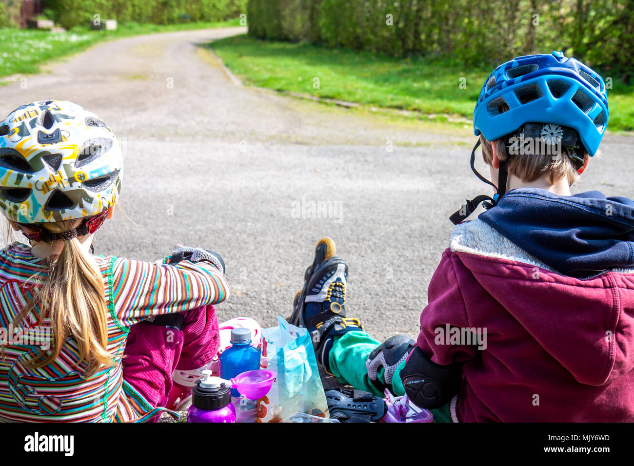Boy and girl wearing rollerblades sitting and eating and drinking