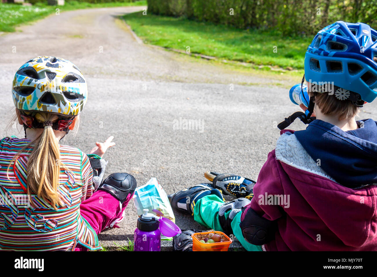 Boy and girl wearing rollerblades sitting and eating and drinking