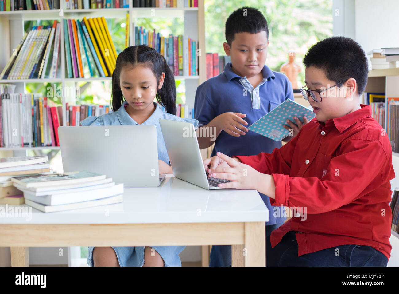 Attentive schoolkid is doing his homework in libary at school. Attentive students  something in their laptop  while sitting at desks in the libry. Bac Stock Photo