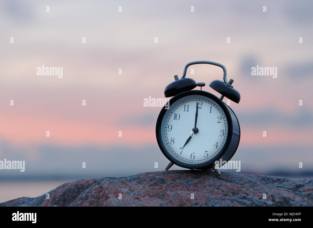 One black alarm clock on rock at seven o clock outdoor during sunrise Stock  Photo - Alamy