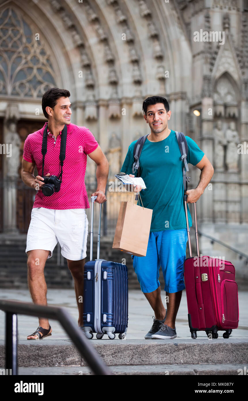 Two men are walking with baggage and watching to sights in Barcelona ...