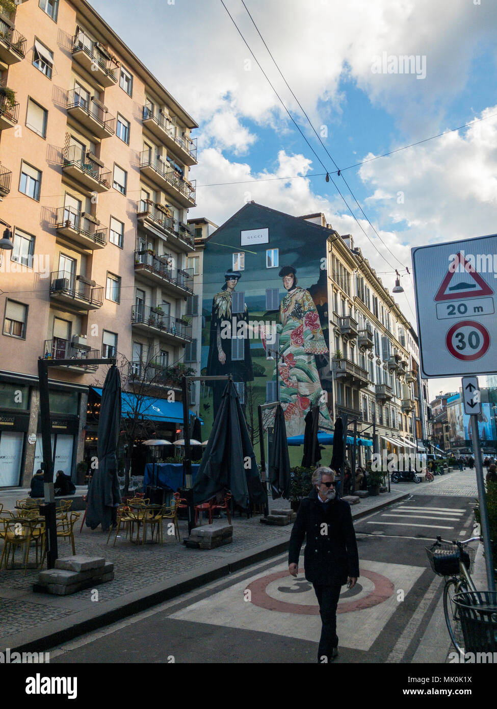 Hipster man walks the streets of downtown Milan, Corso Garibaldi, Italy. Behind him, you can see the Gucci advertising poster painted on the wall Stock Photo