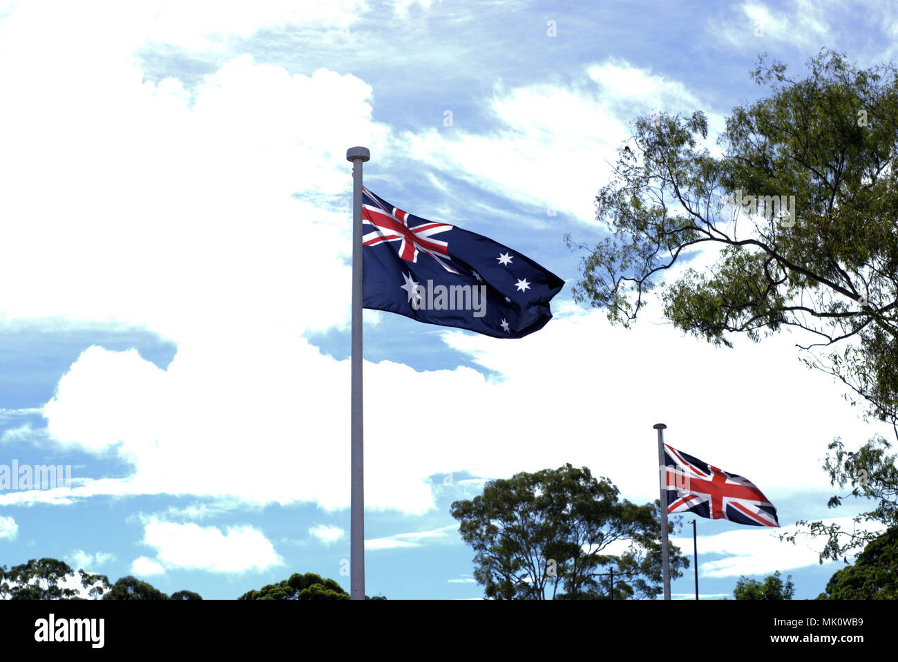 Flying Australian flag and British flag in background on ANZAC day. Waving flags of Australia and England with blue sky and white clouds. Stock Photo