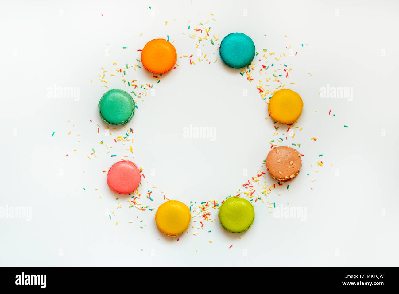 Top view of colorful macaroons and sugar sprinkles arranged in circle over white background. Copy space. Stock Photo
