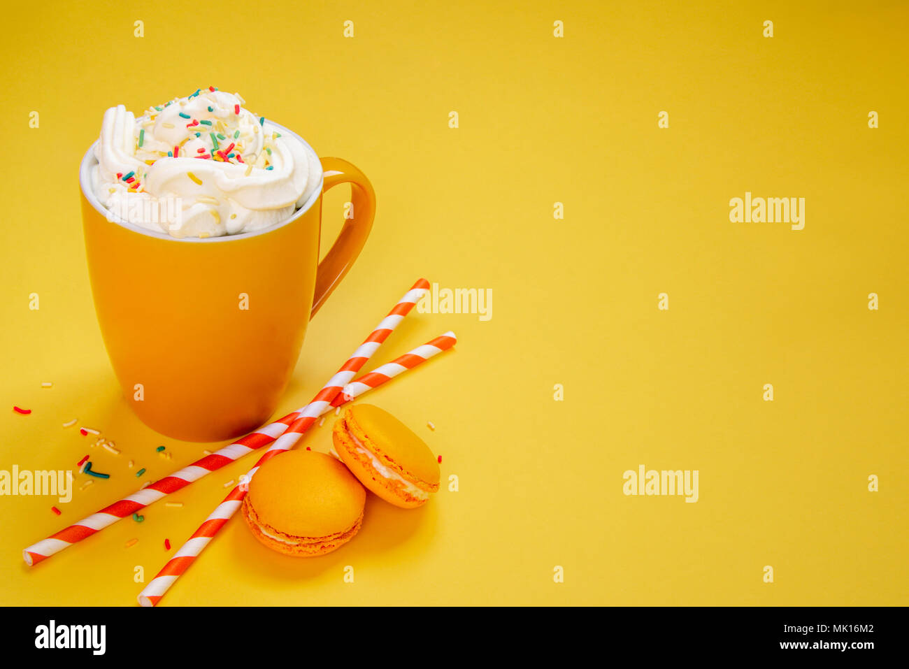 Close up of yellow coffee cup, straws and french macaroons over yellow background. Stock Photo