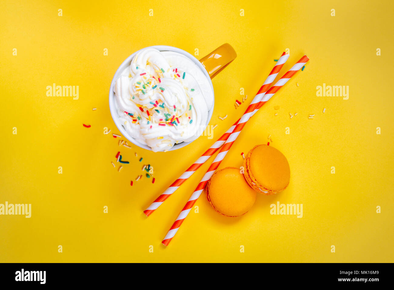 Top view of yellow coffee cup, straws and french macaroons over yellow background. Stock Photo