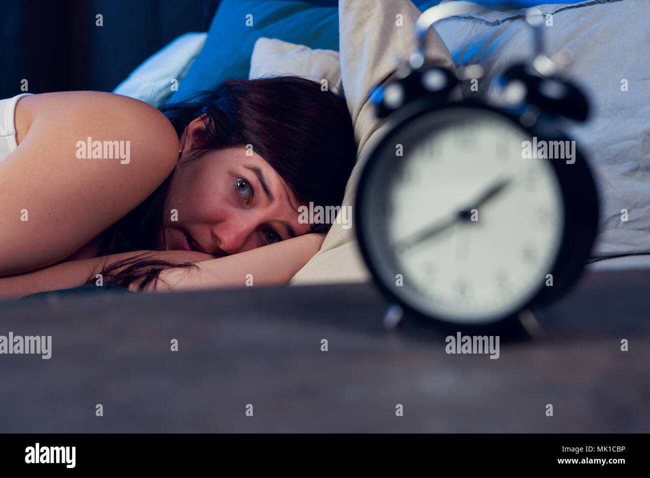 Image of with insomnia lying on bed next to alarm clock at