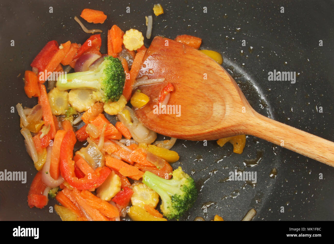 Closeup of stir fried vegetables in a wok with a wooden spoon Stock Photo