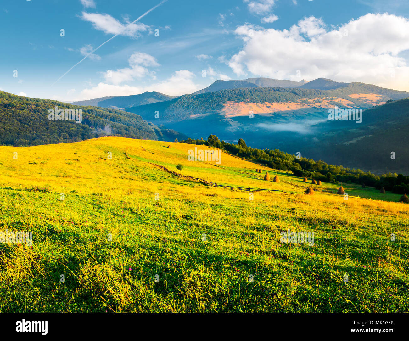 beautiful rural scenery in mountains at sunrise. haystacks on the field behind the fence. outdated agriculture technology concept Stock Photo
