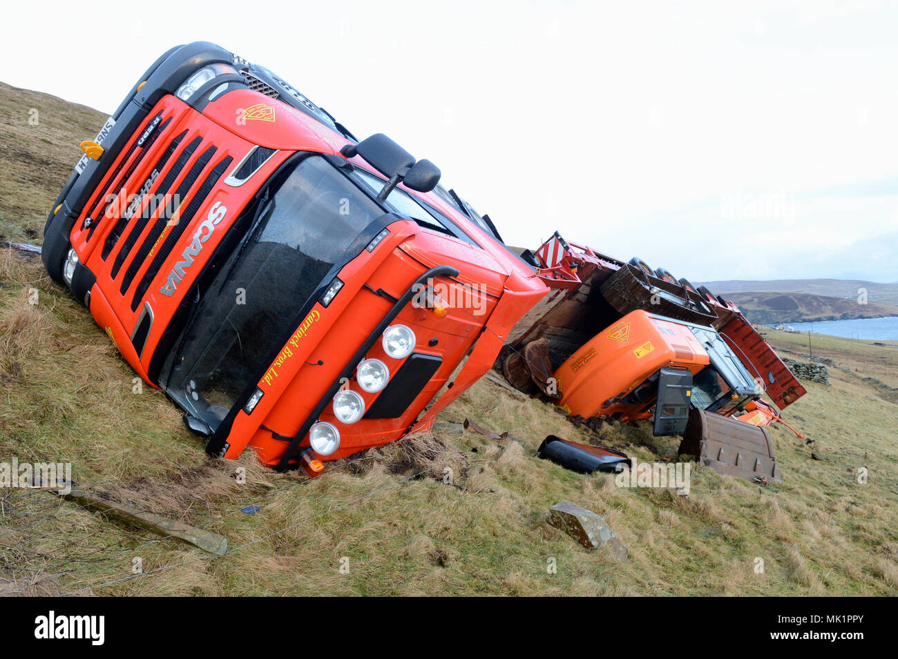 Articulated lorry and trailer with digger lying in ditch on side of road after accident on main road Stock Photo