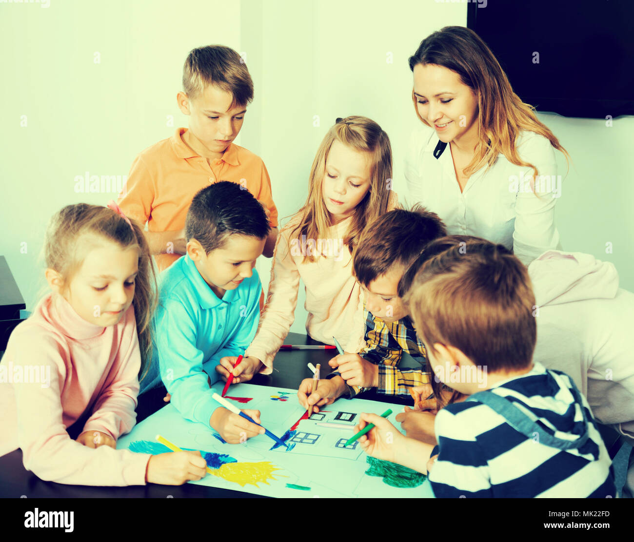 Happy team of elementary age children and female teacher drawing on one ...