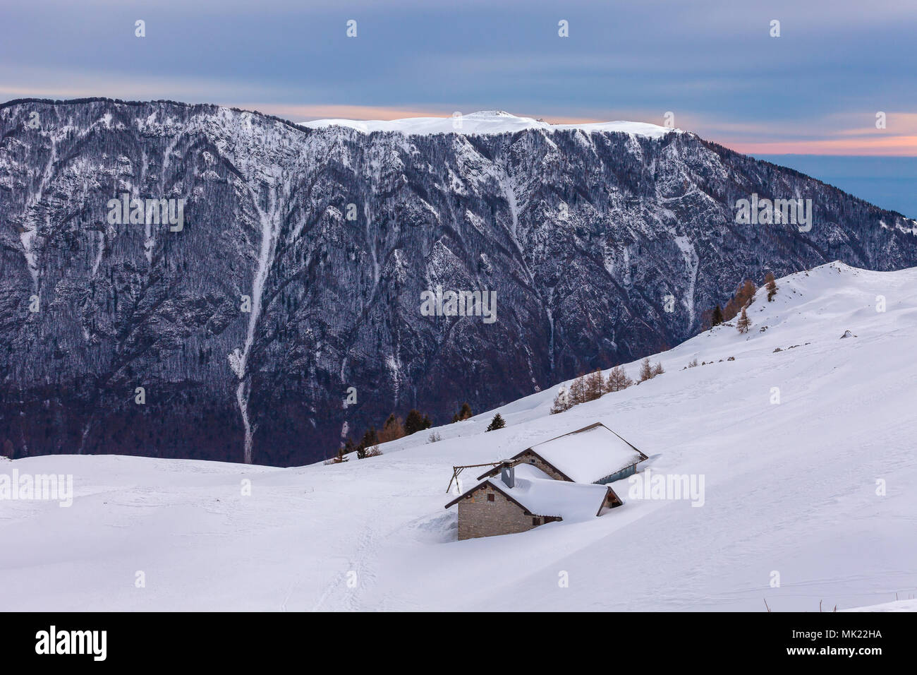 Small mountain farmhouses on snowy slope with, mountain and forest  background, Belluno, Veneto, Italy Stock Photo
