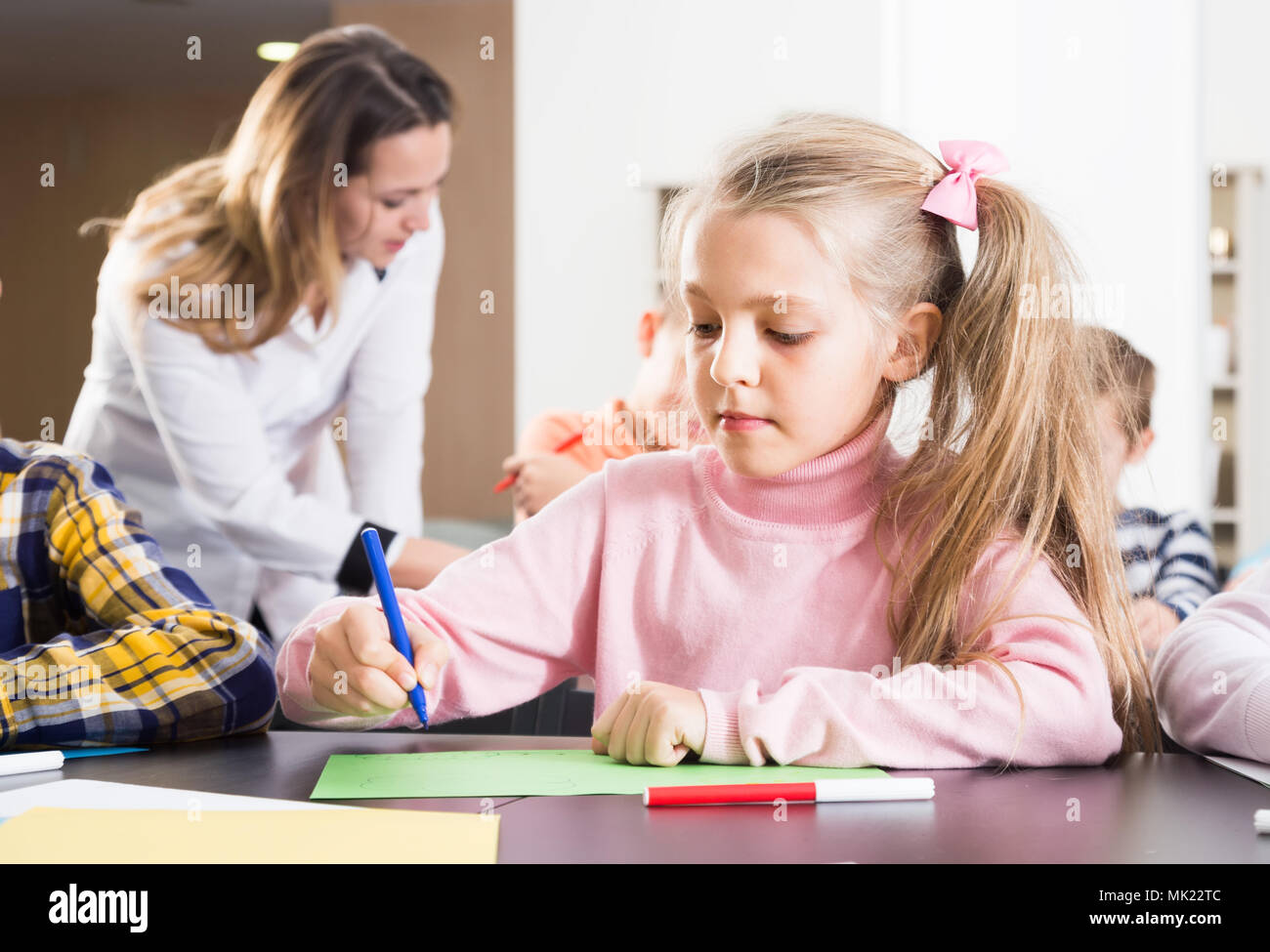 Female teacher and elementary age children drawing at class in school ...