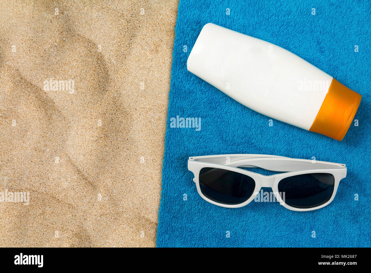 Towel on a sandy beach with a pair of sunglasses and a bottle of suntan cream from overhead with copy space for additional messages Stock Photo