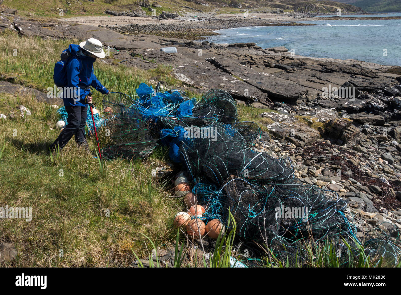Walker examining discarded plastic and nylon fishing gear on Scottish beach, Isle of Skye, Scotland, UK Stock Photo