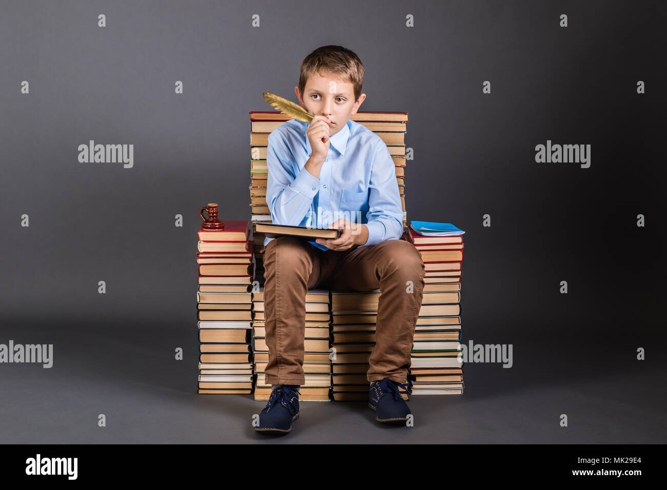 Education concept. A boy with quill pen sits on a throne of books Stock Photo
