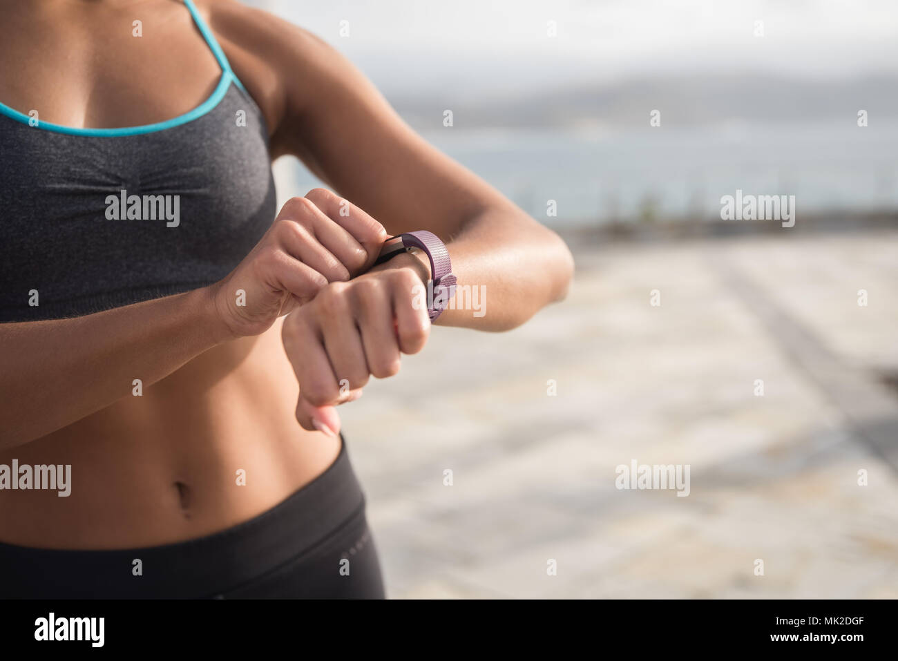 A woman in fitness clothing touching her smartwatch with her midriff and chest in the image and the sea in the background Stock Photo