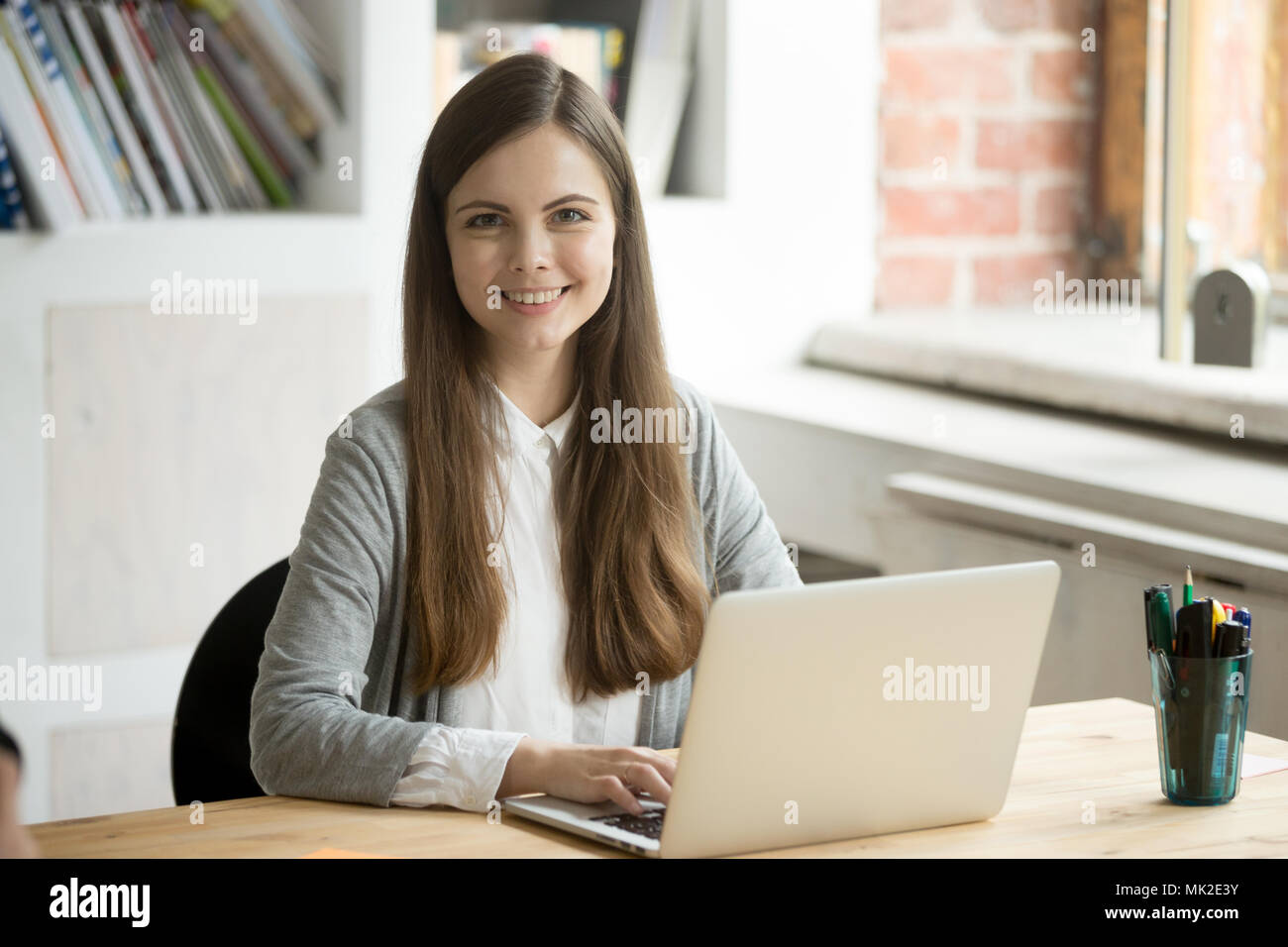 Smiling female worker posing while working at laptop Stock Photo