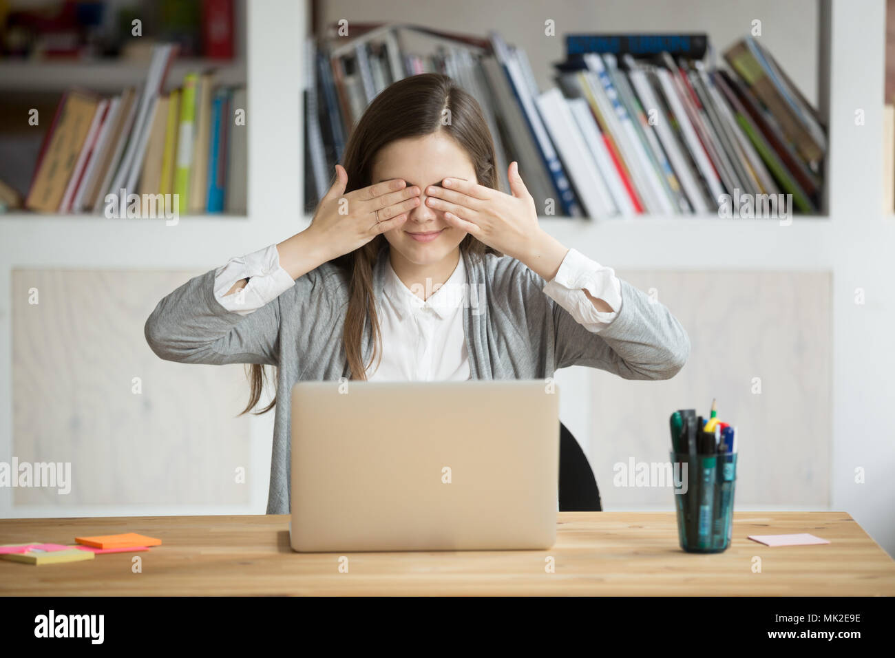 Young female worker playing childish covering eyes with hands Stock Photo