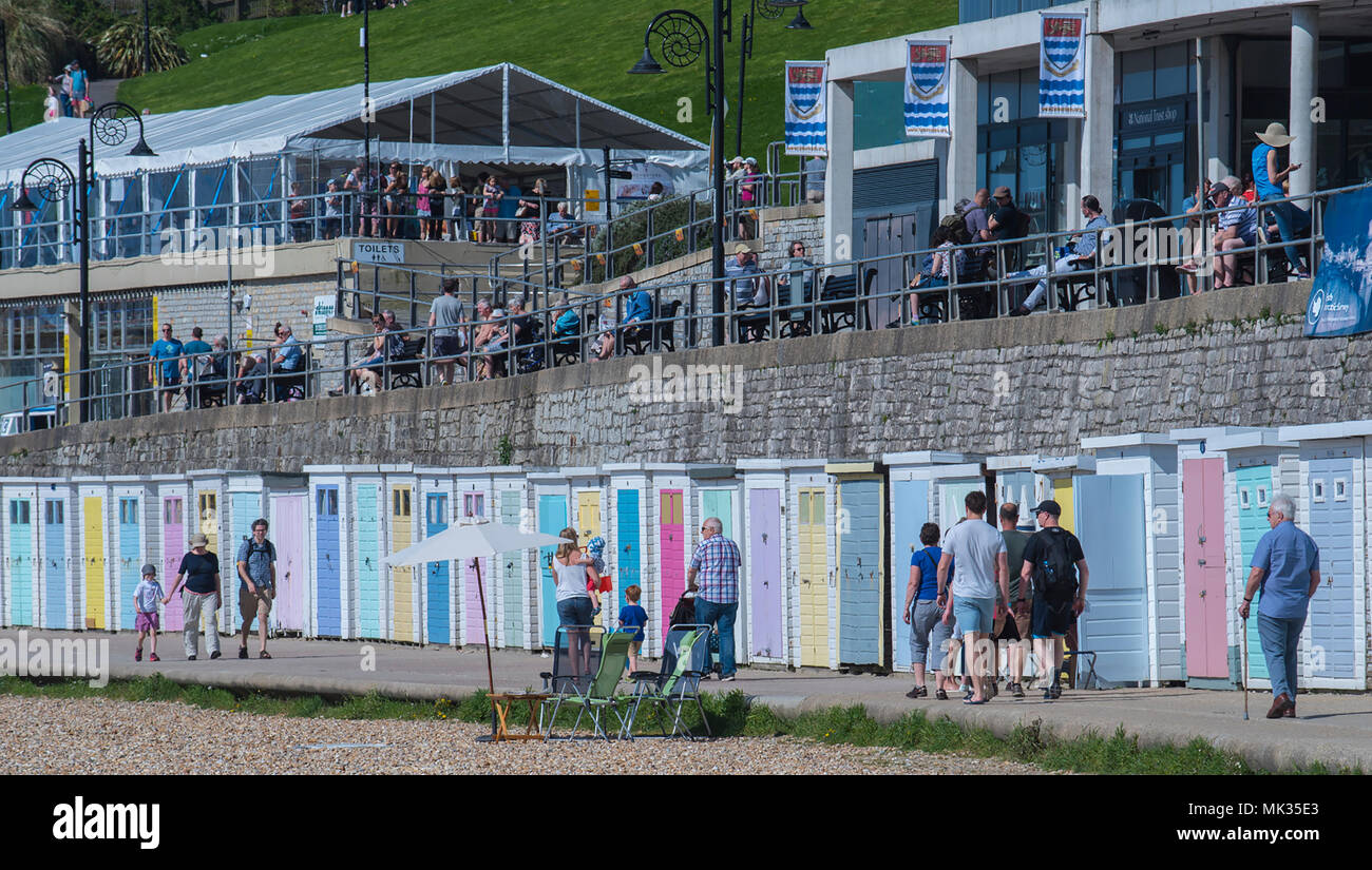 Sun in Lyme Regis, Dorset, UK. 6th May 2018. UK Weather: Visitors stroll past the beach huts on Marine Parade as the south coast  resort town of Lyme Regis hosts the annual Fossil Festival under blue sky and warm sunshine on the May bank holiday weekend. Credit: PQ/Alamy Live News Stock Photo